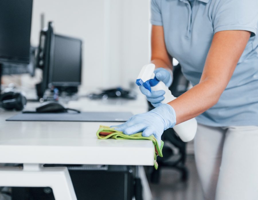 Close up view of woman in protective gloves that cleaning tables in the office.